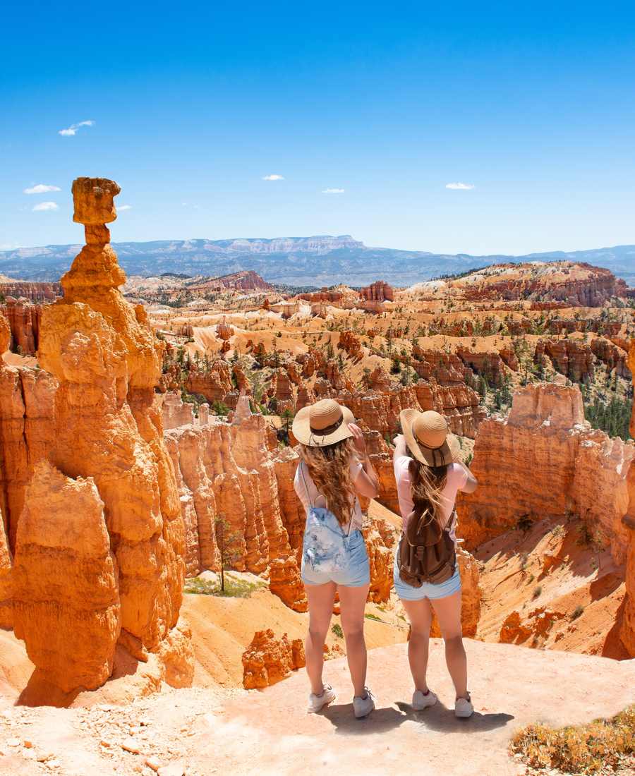 Twee meisjes met een zonnehoed kijken uit over de hoodoos van Bryce Canyon, Utah, Amerika