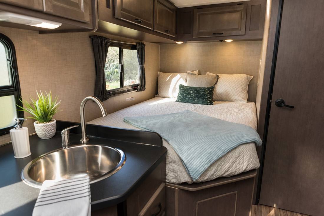 Het vaste bed achterin een compacte huurcamper, met het keukentje ervoor, Amerika