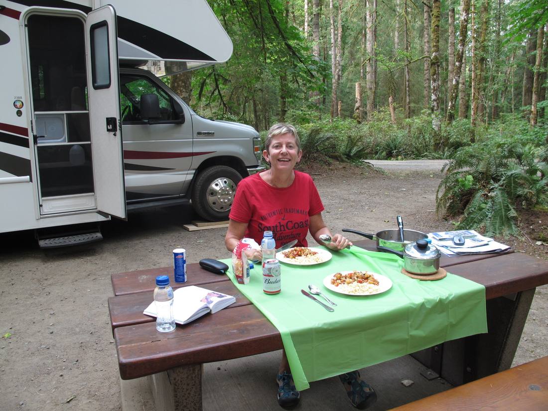 Een vrouw eet aan de picknicktafel naast de camper op een boscamping, Amerika
