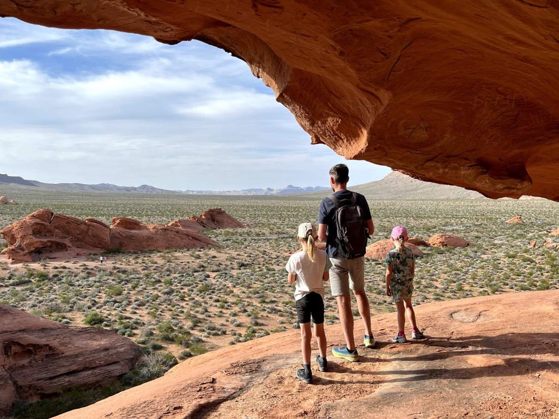 Een vader met twee kinderen onder een rode rotsboog in Valley of Fire, Nevada, Amerika