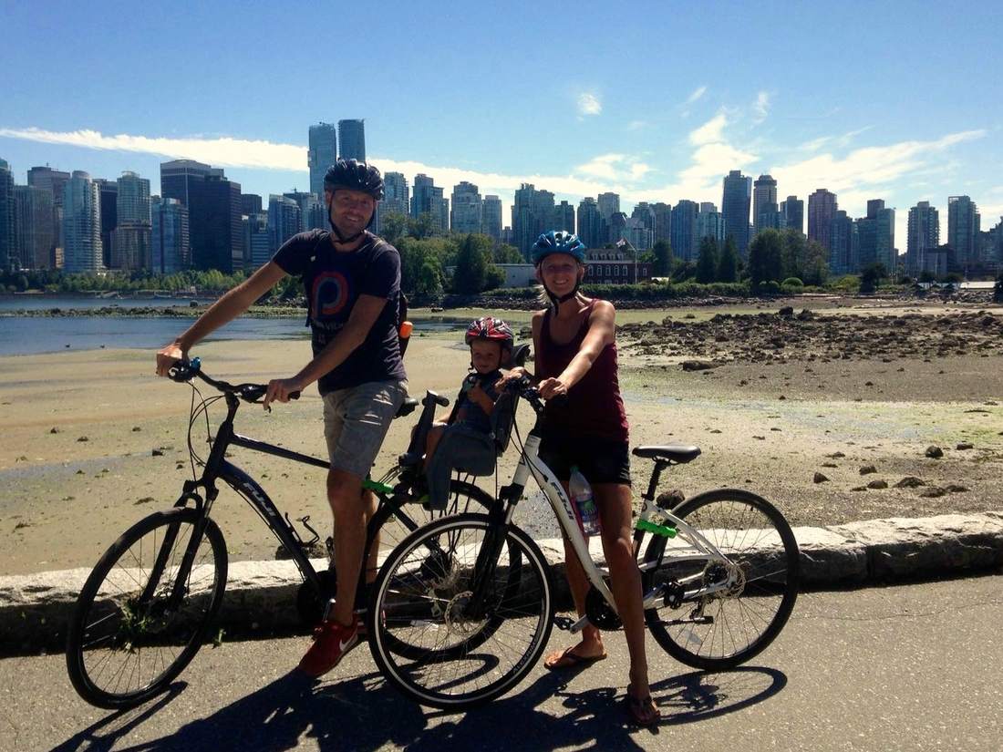 Een gezin op de fiets langs het water met de skyline van Vancouver erachter, British Columbia, West-Canada