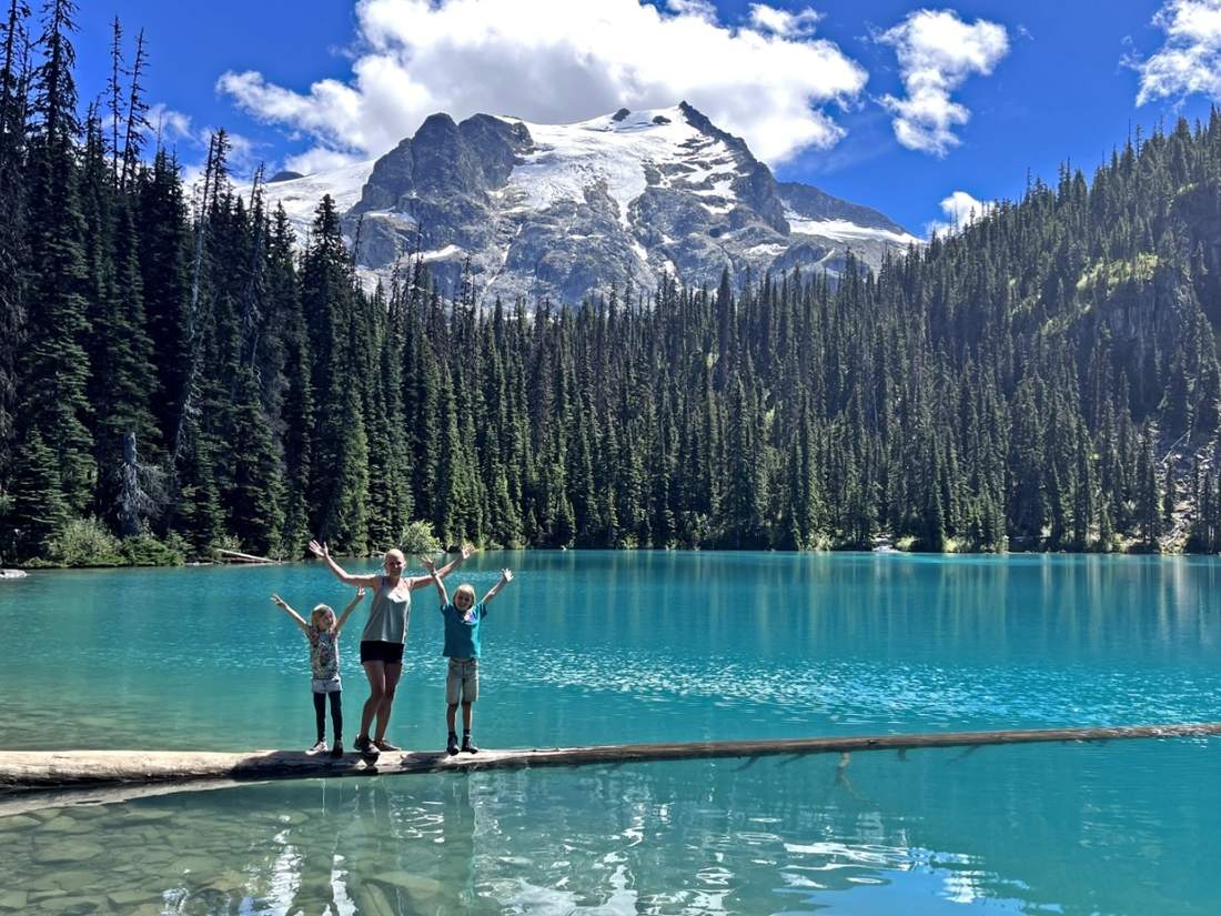 Kinderen op een boomstam in het turquoise water van Joffre Lakes, British Columbia, West-Canada