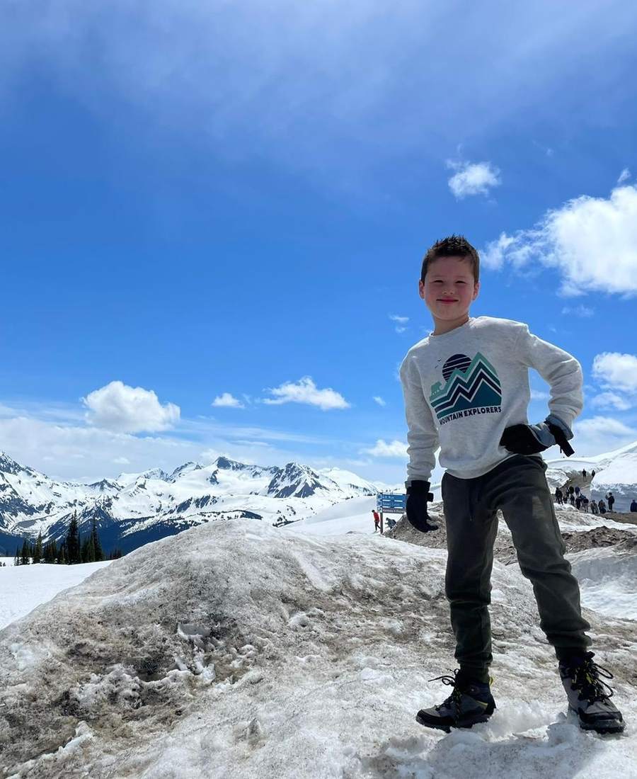 Een jongen staat in de sneeuw met besneeuwde bergtoppen erachter, West-Canada