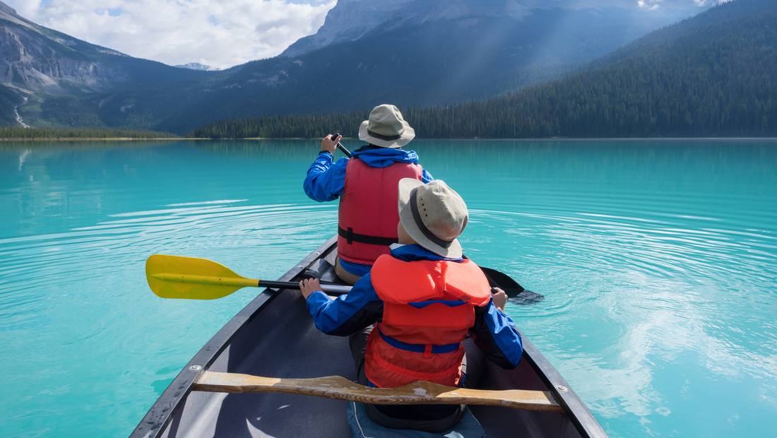 Twee kinderen met zwemvest peddelen in een kano over een turquoise bergmeer in de Rockies, West-Canada