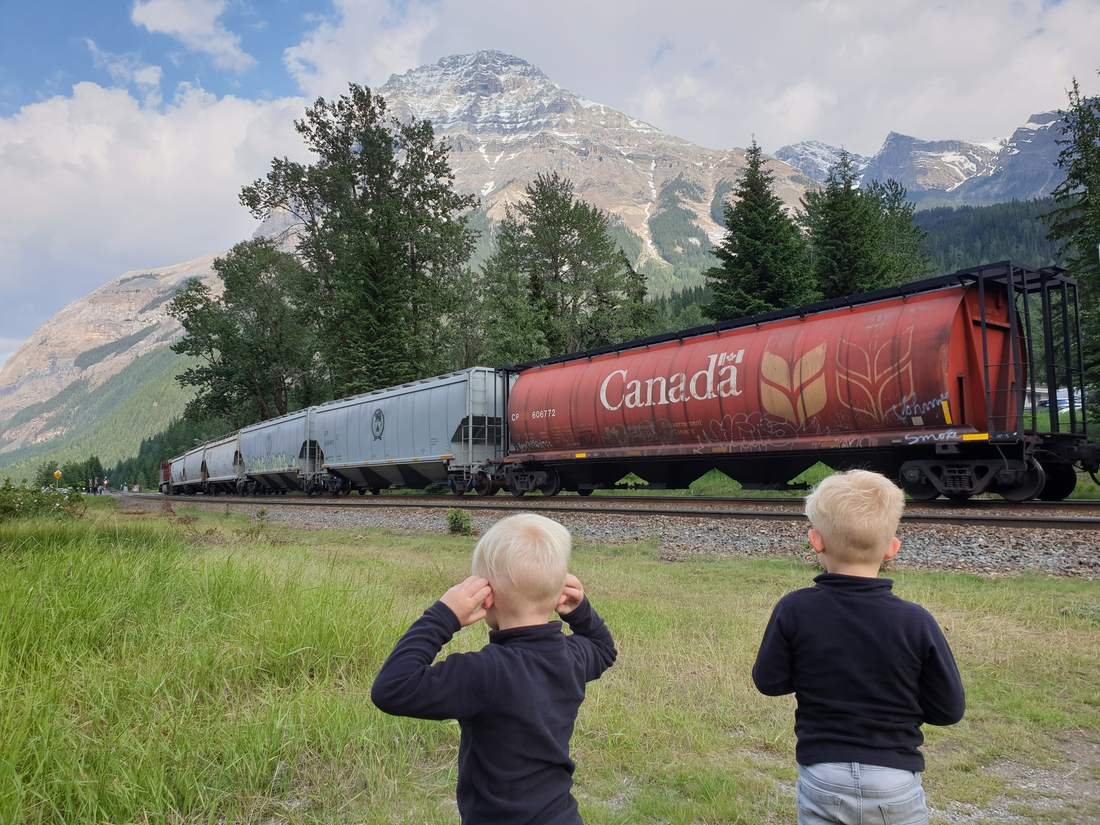 Twee jongetjes kijken naar een lange goederentrein door de Rockies, West-Canada