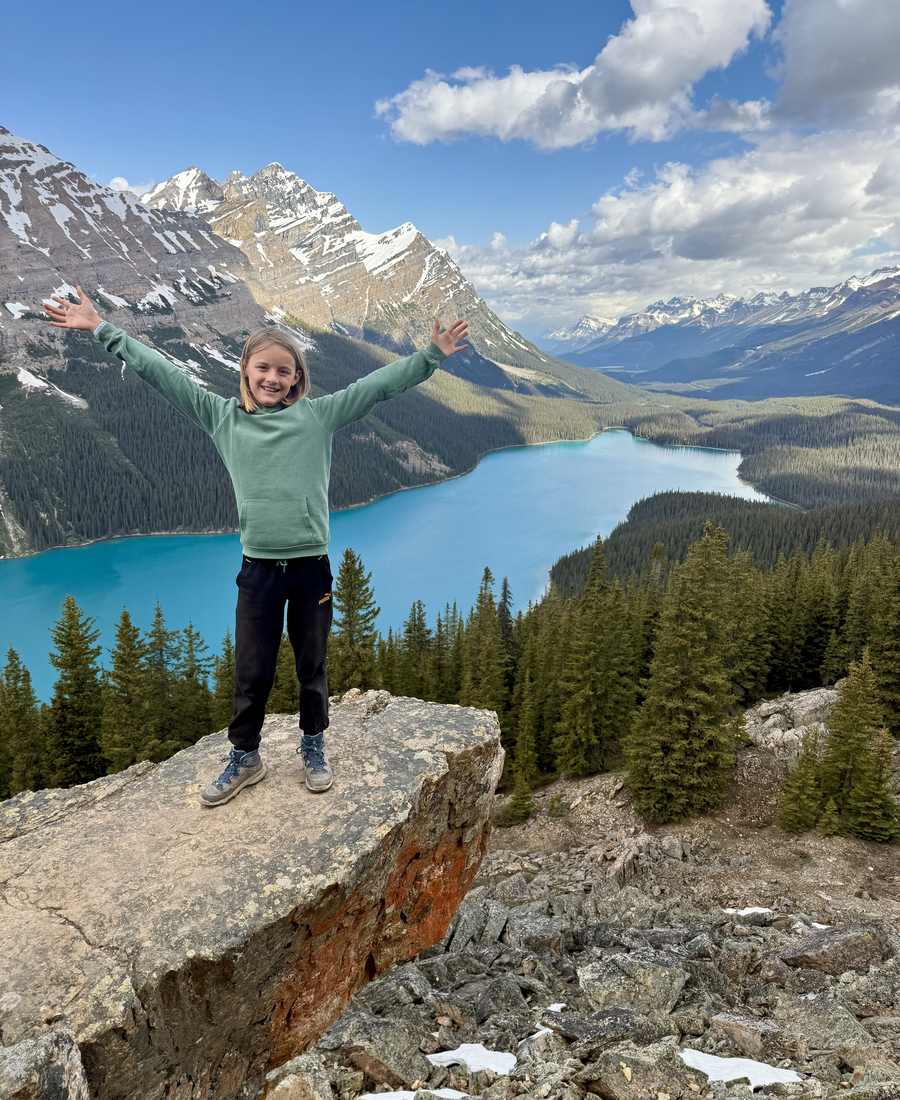 Een meisje met de armen omhoog op een rots boven het turquoise Peyto Lake, Icefields Parkway, Alberta, West-Canada