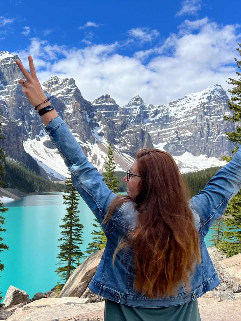 Reiziger juicht met de armen omhoog bij het turquoise Moraine Lake, Alberta, West-Canada