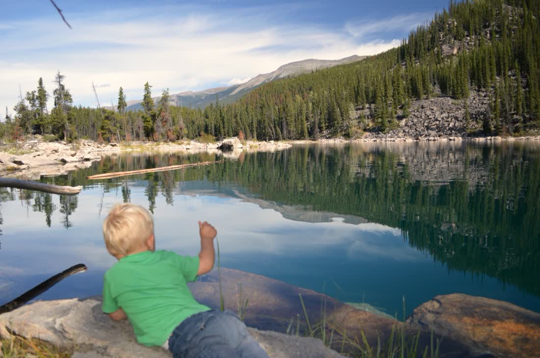 Kind speelt aan de rand van een bergmeer, West-Canada