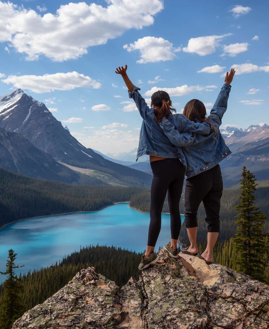 Een stel steekt de armen omhoog op een rots boven een turquoise bergmeer in de Rockies, West-Canada