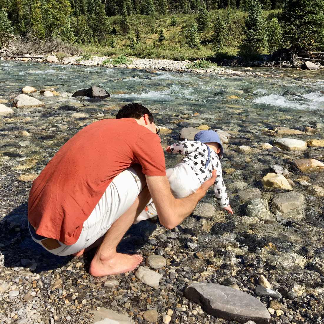 Een vader en zijn peuter spelen met stenen aan de rand van een bergrivier, British Columbia, West-Canada