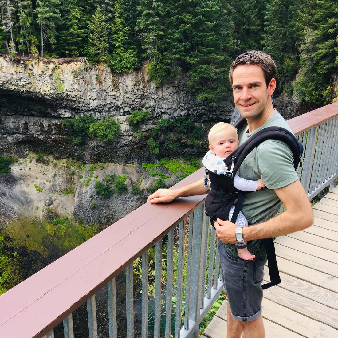 Een vader met zijn baby in de draagzak op een brug boven een kloof in de Rockies, West-Canada