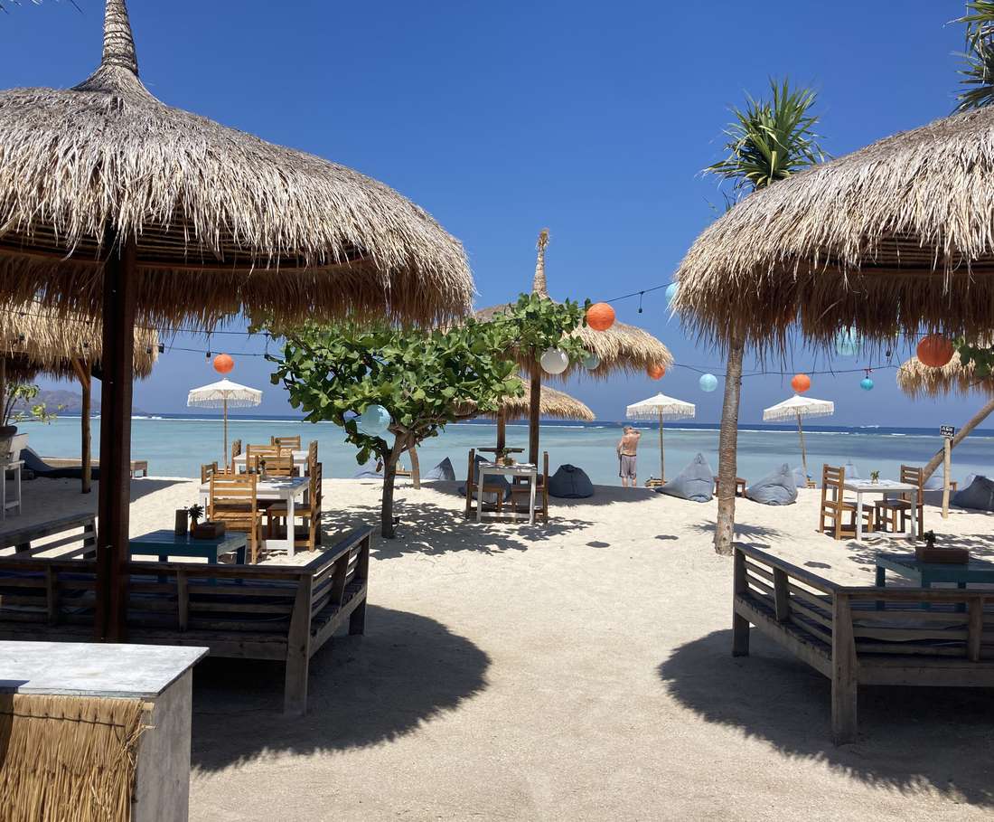 Strandbedden onder rieten parasols staan vlak aan het heldere water van Gili Air, Indonesië