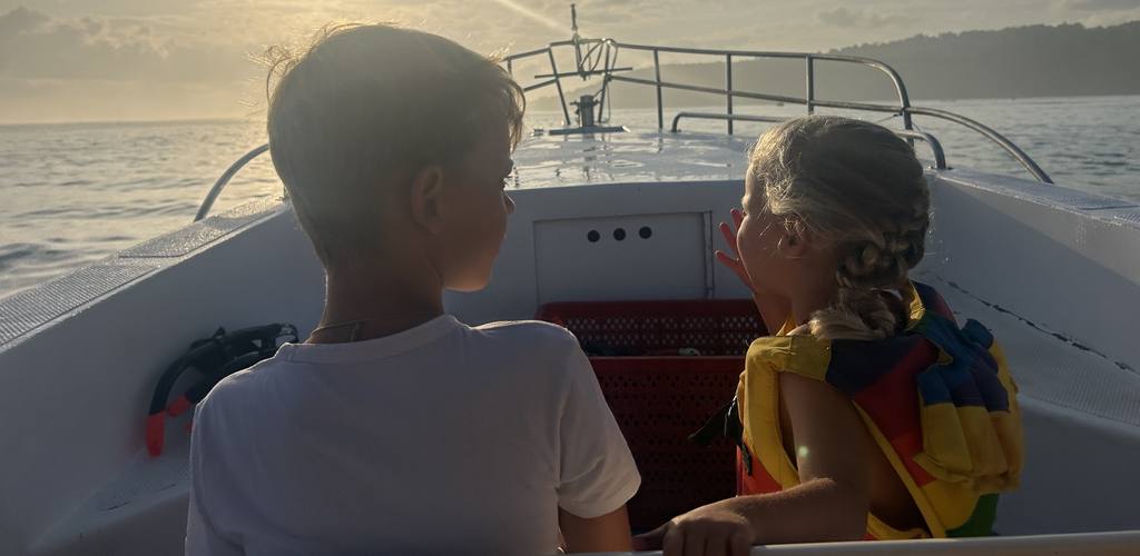 Twee kinderen kijken vanaf de boot uit over zee bij zonsopkomst, Indonesië