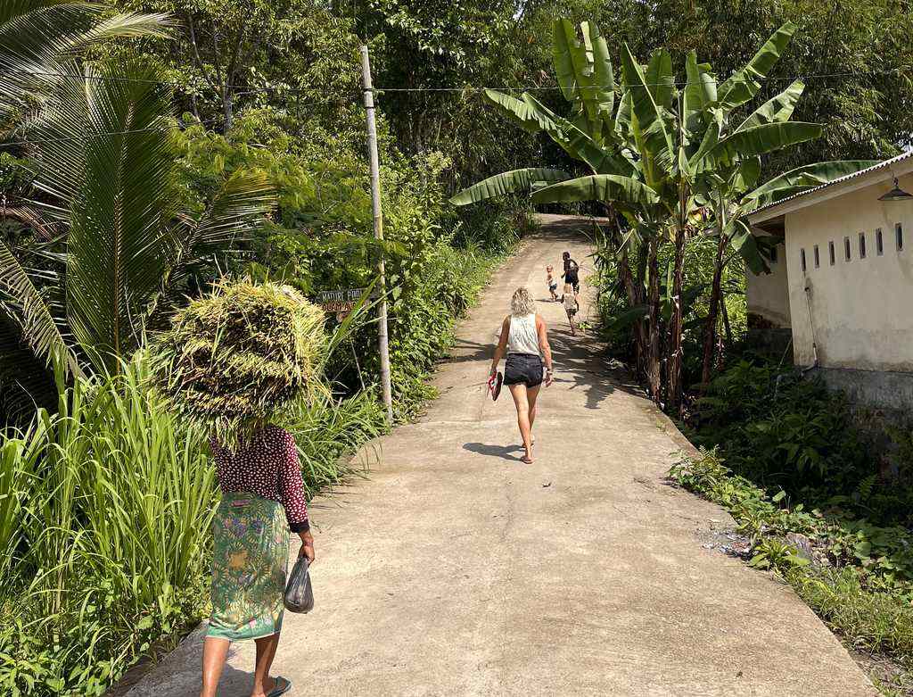 Vrouw draagt rijst op haar hoofd over een dorpspad op Lombok, Indonesië