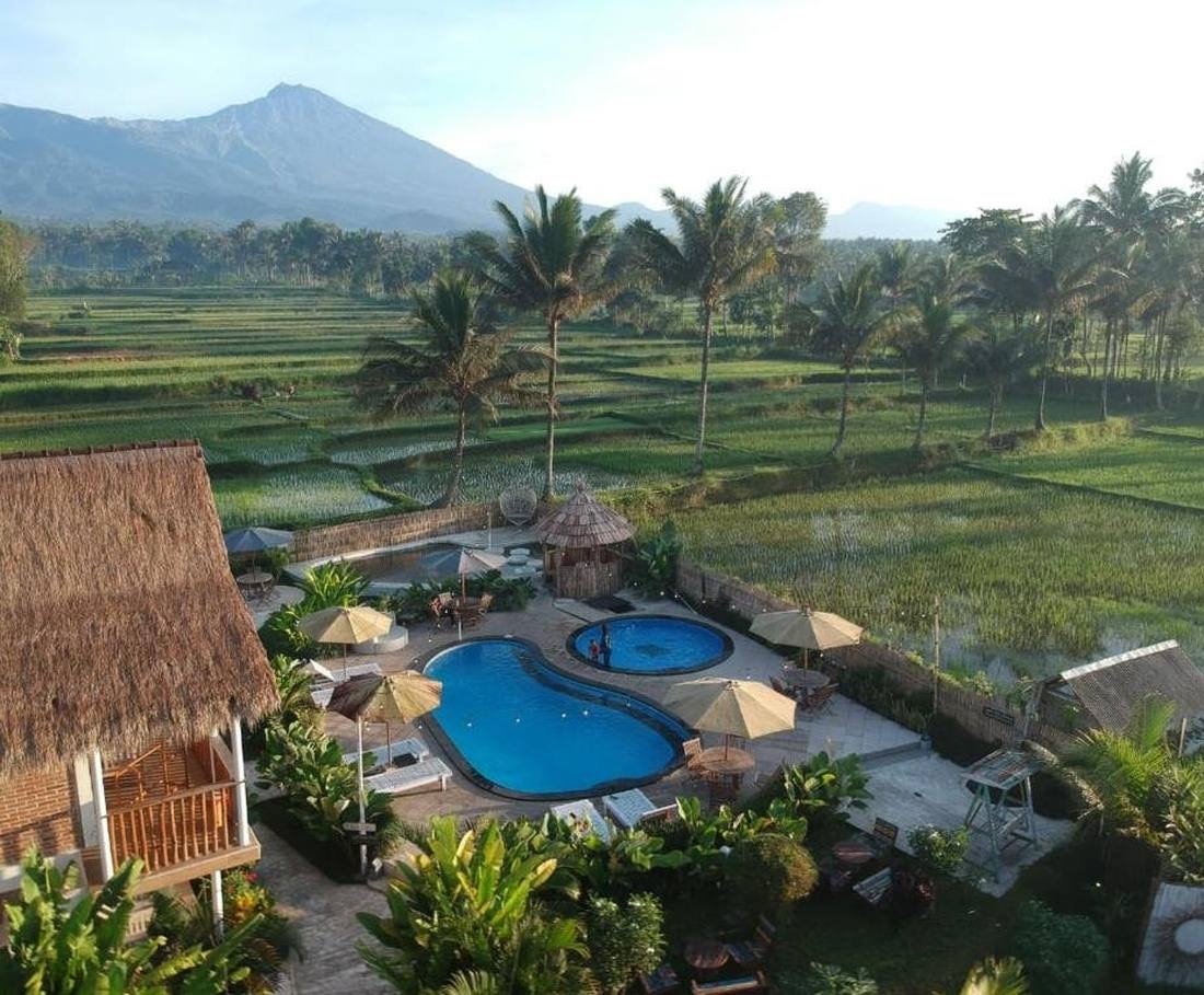 Het zwembad en de bungalows tussen de rijstvelden bij Tetebatu op Lombok, met de Rinjani erachter, Indonesië