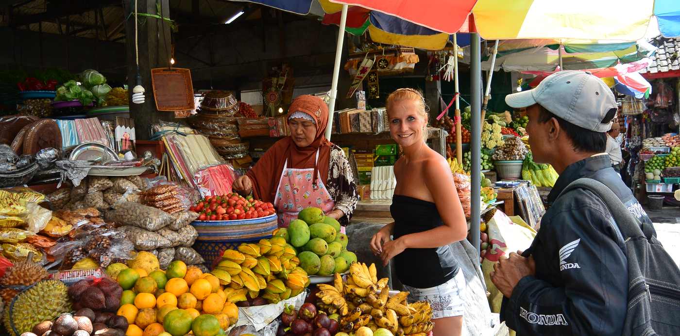 Een reizigster koopt fruit op de markt onder de gekleurde parasols, Indonesië