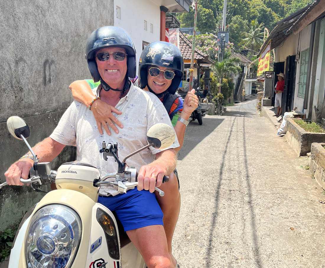 Twee reizigers rijden op een scooter door de smalle dorpsstraat van Munduk, Bali