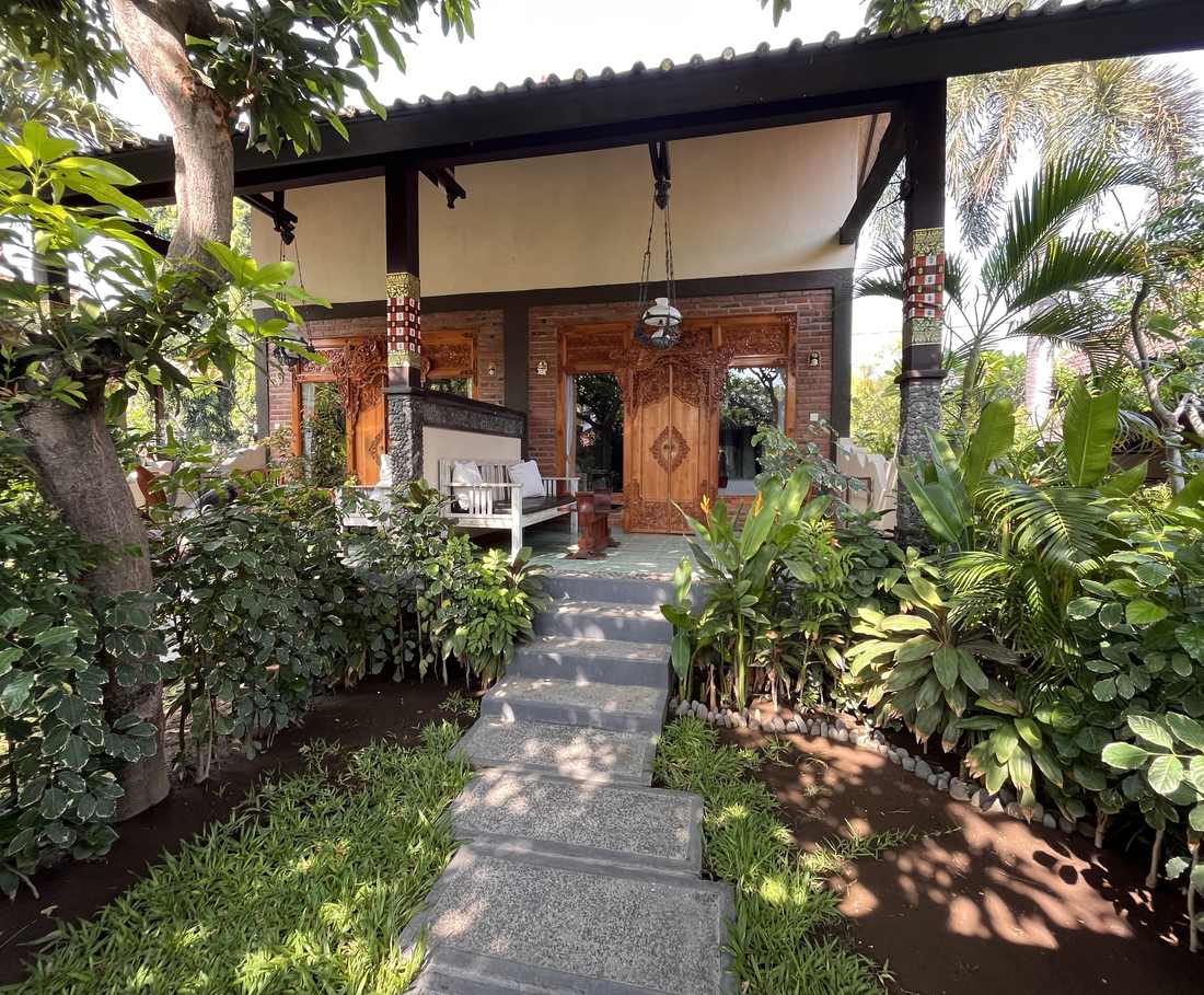 Een houten bungalow met gesneden deur staat tussen het groen in Pemuteran, Bali