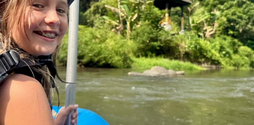 Tiener met zwemvest en peddel in een blauwe raft op de rivier bij Ubud, Bali, Indonesië