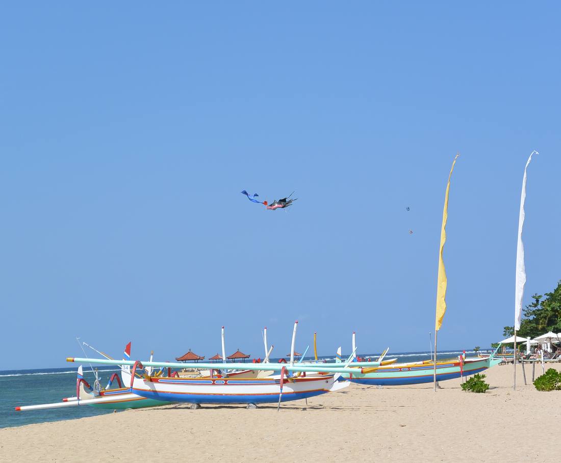 Kleurrijke vissersboten op het strand van Sanur, met een vlieger in de lucht, Bali