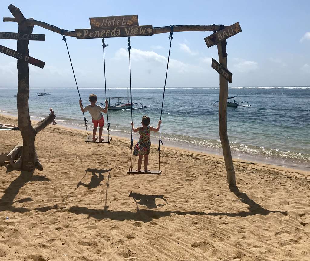 Kinderen op een schommel aan het strand met vissersboten op de achtergrond, Indonesië