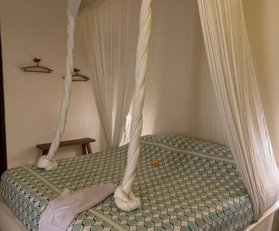 Een bed met klamboe in een kamer met veel hout en natuurlijke kleuren, Uluwatu, Bali