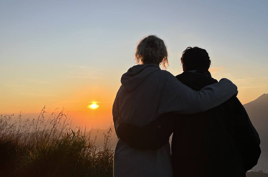 Twee reizigers kijken met een arm om elkaar heen naar de zonsopkomst boven op de vulkaan, Bali, Indonesië