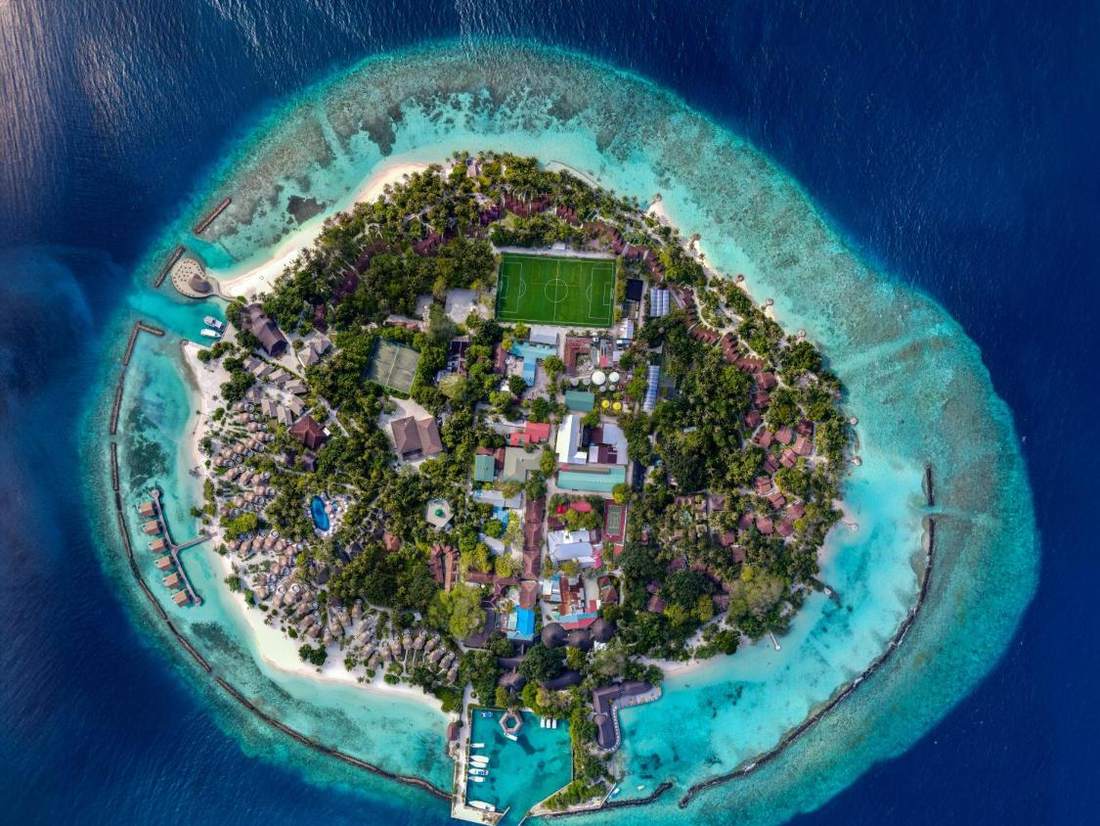 Een rond resorteiland met een rif eromheen, van boven gezien, de Malediven