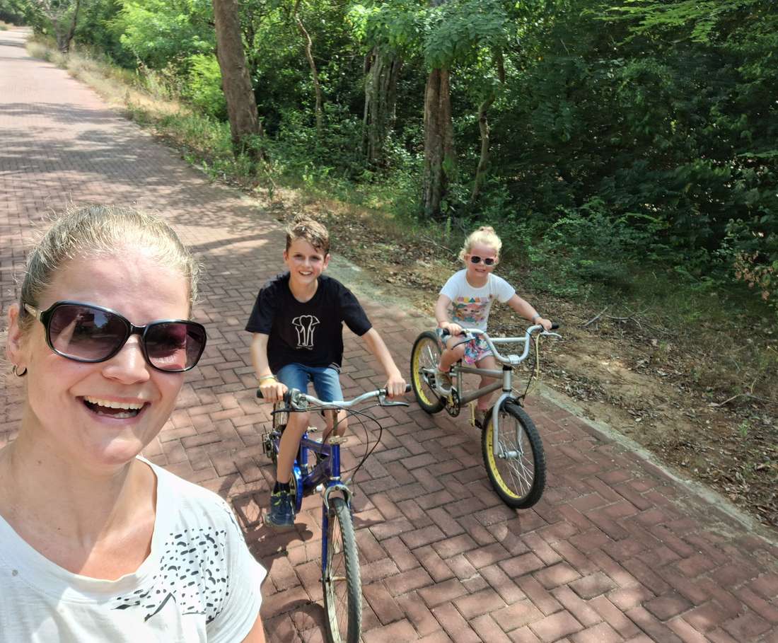 Een moeder fietst met haar twee kinderen over het klinkerpad door het groen van Polonnaruwa, Sri Lanka