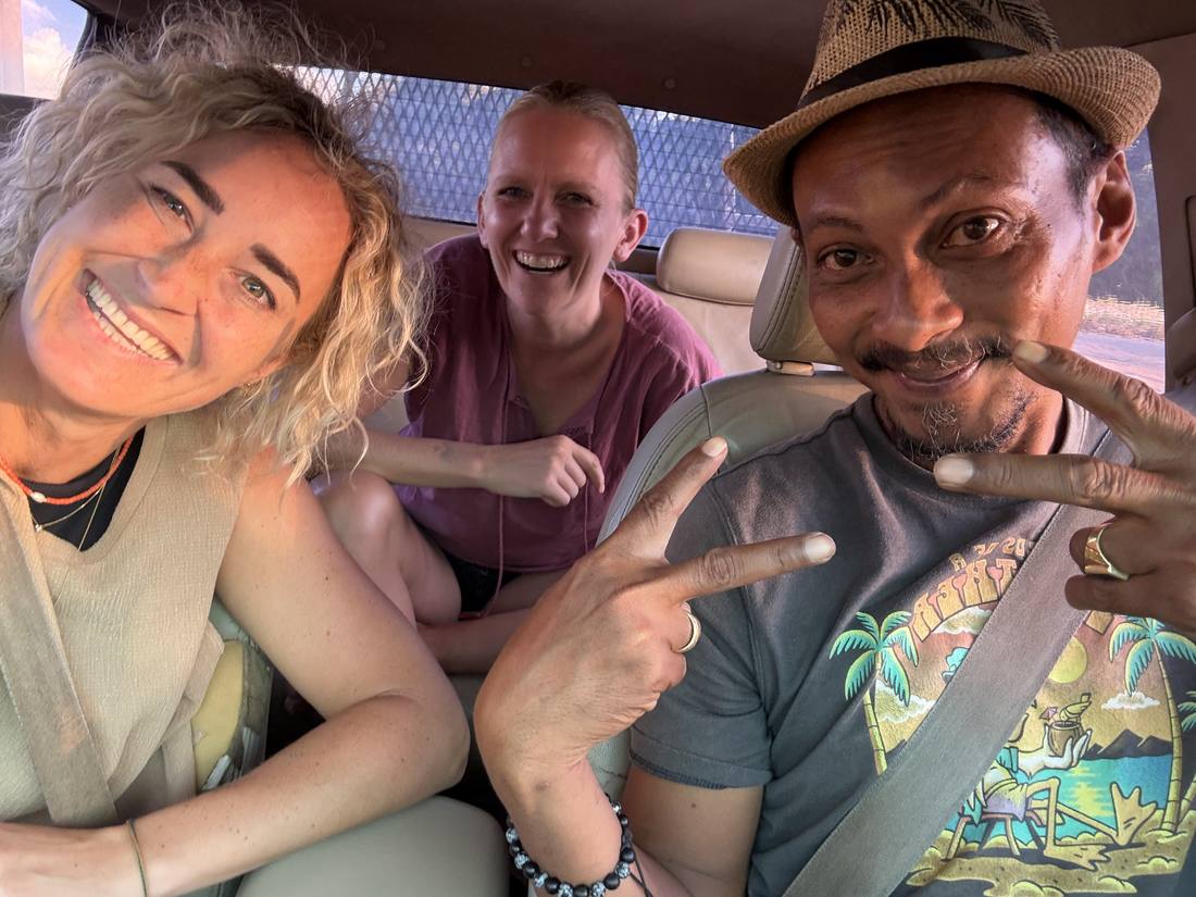Nynke en Ilse op de achterbank, met hun chauffeur die naar de camera lacht