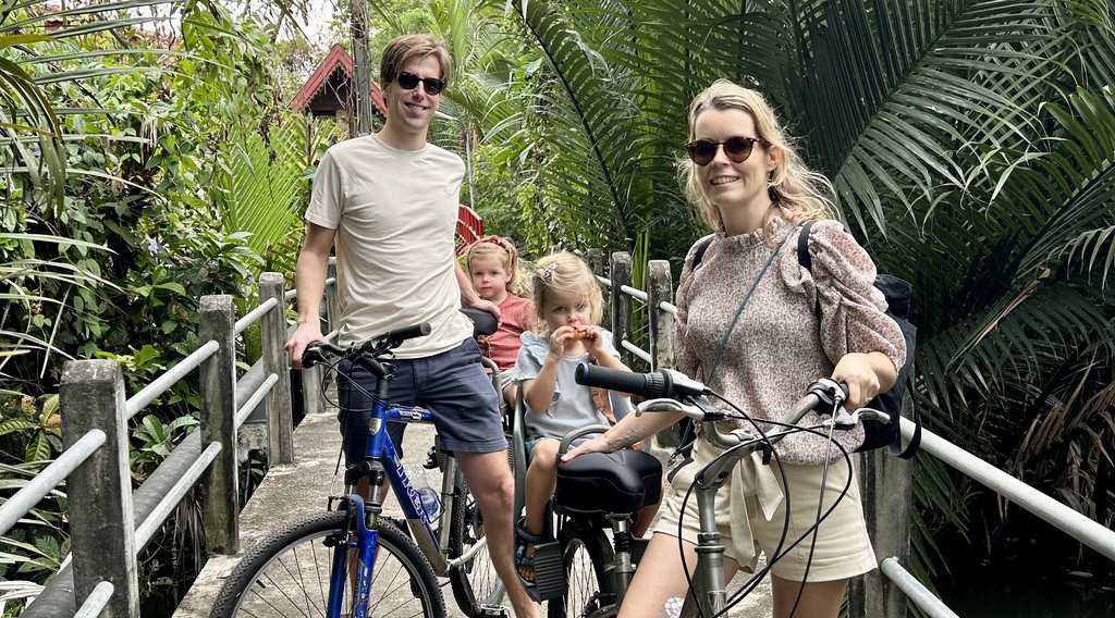 Een gezin op de fiets over een bruggetje tussen de palmen in Bangkok, Thailand
