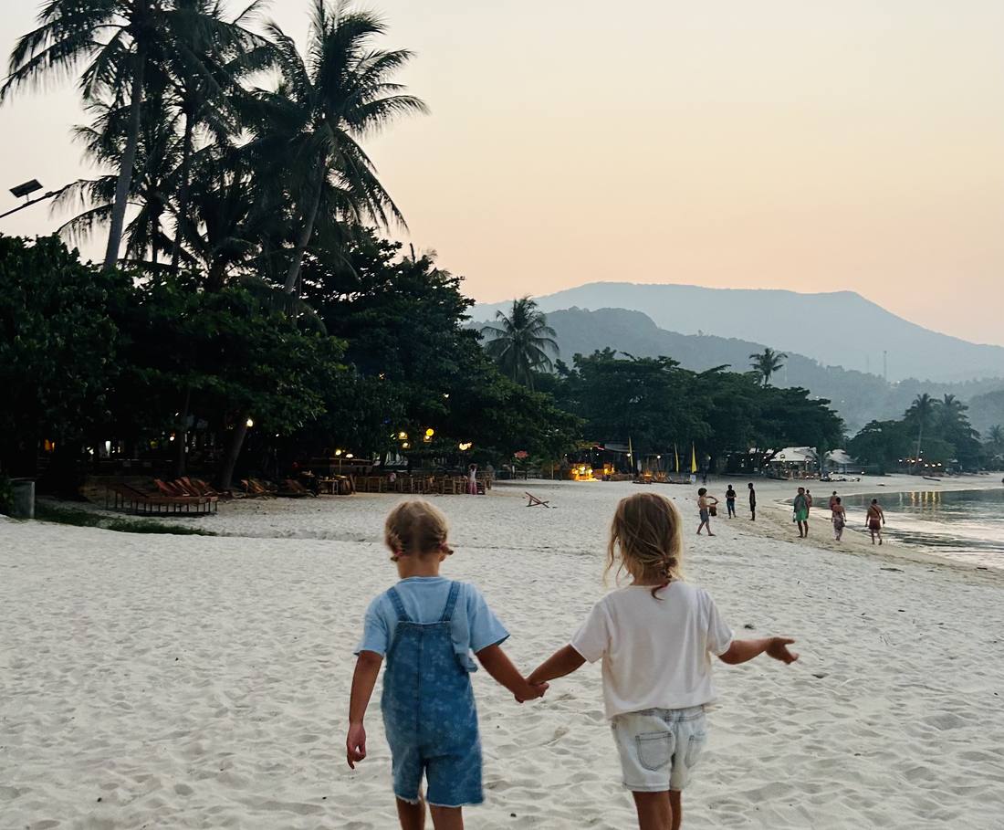 Twee peuters lopen hand in hand over het strand bij zonsondergang in Thailand