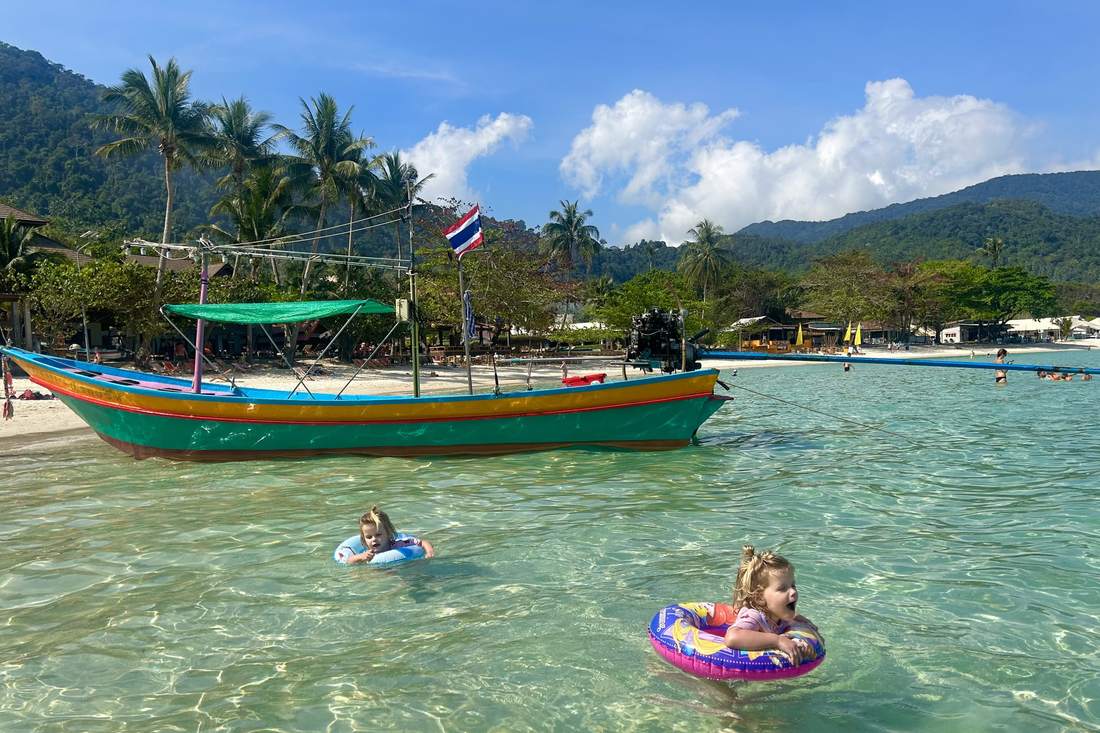 Twee peuters dobberen in zwembanden naast een longtailboot in Thailand