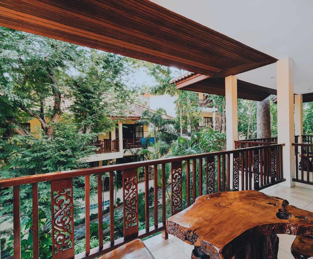 Een houten veranda met gesneden balustrade kijkt uit op het groen van Koh Phangan, Thailand