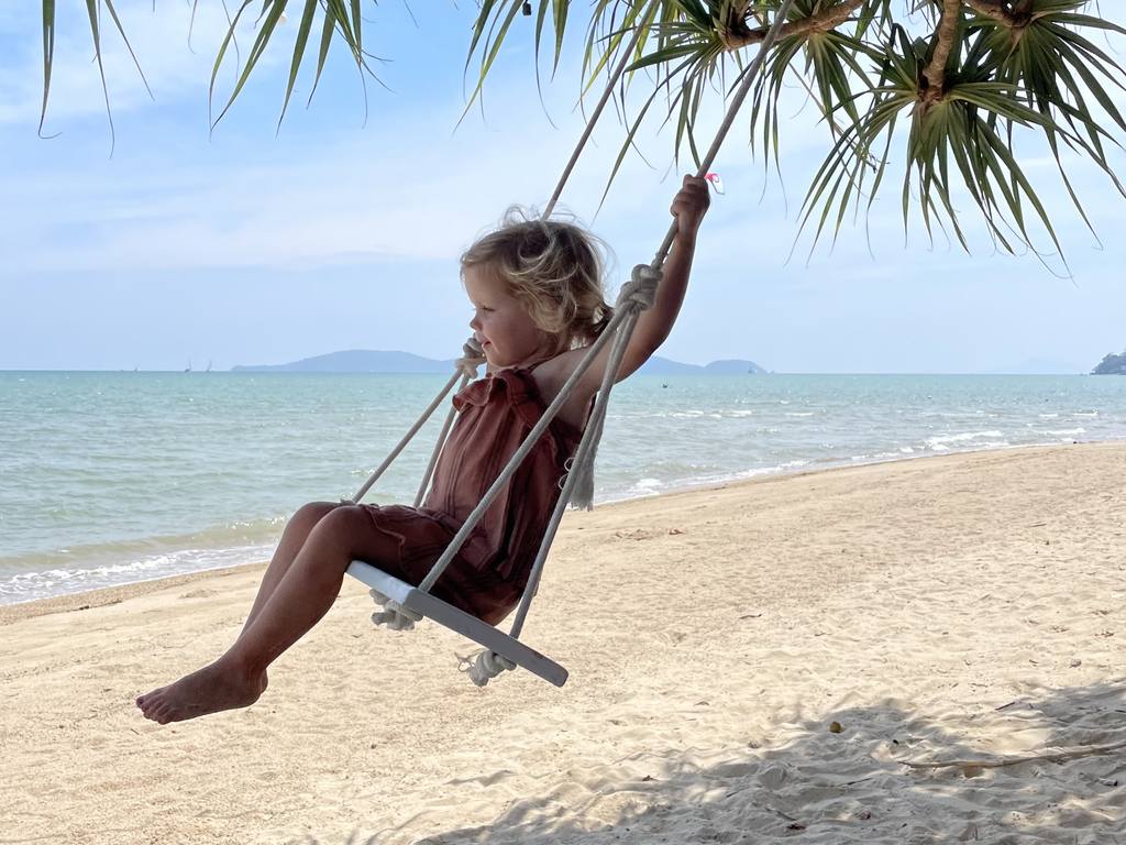 Een kind schommelt aan een boom boven het strand in Thailand
