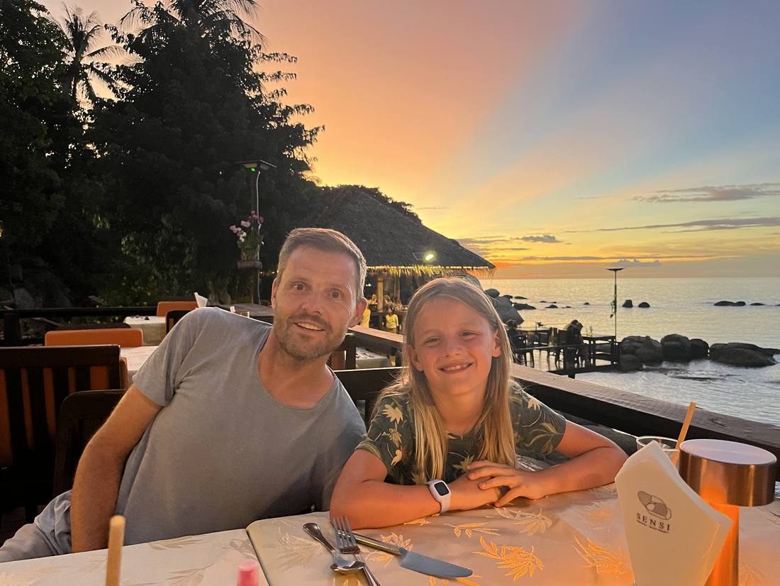 Vader en zoon aan tafel bij zonsondergang aan zee, Thailand