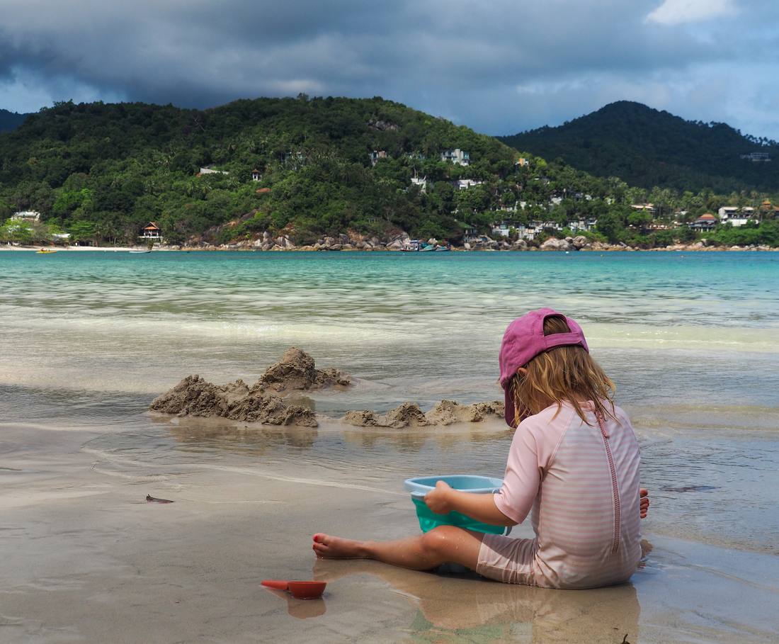 Een peuter bouwt een zandkasteel in het ondiepe water van Koh Tao, Thailand