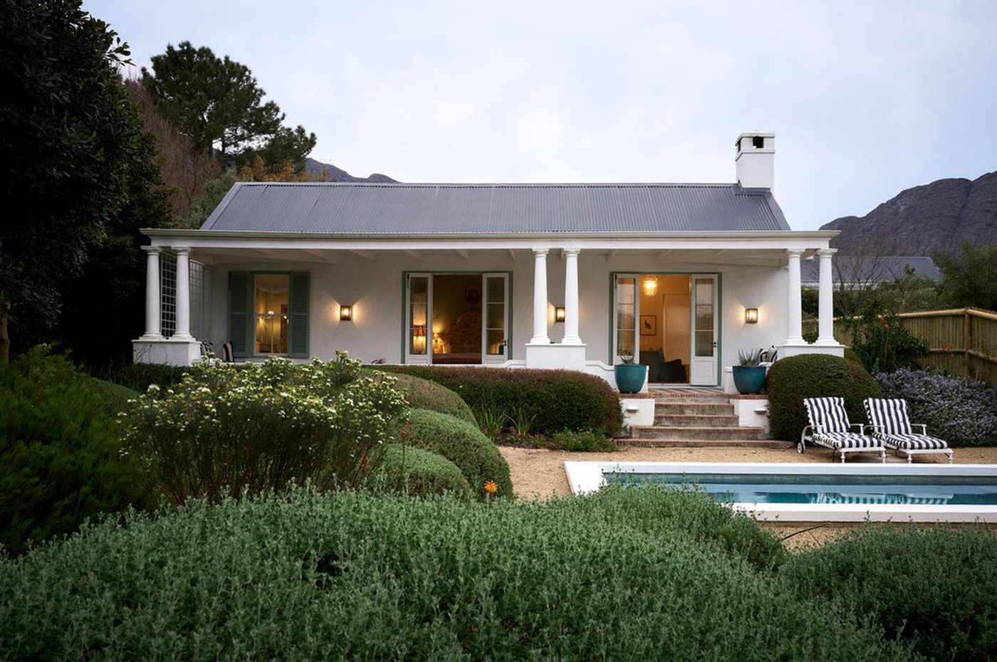 Een wit huisje met een brede veranda op een wijnlandgoed bij Franschhoek, met de bergen erachter, Zuid-Afrika