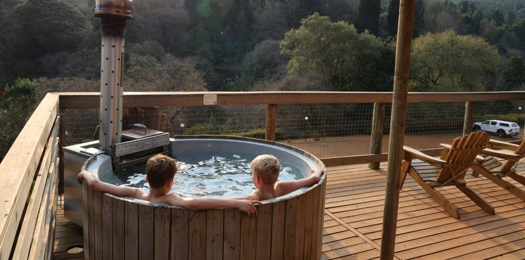 Twee kinderen in een houtgestookte hottub op het terras met uitzicht over de beboste vallei, Zuid-Afrika