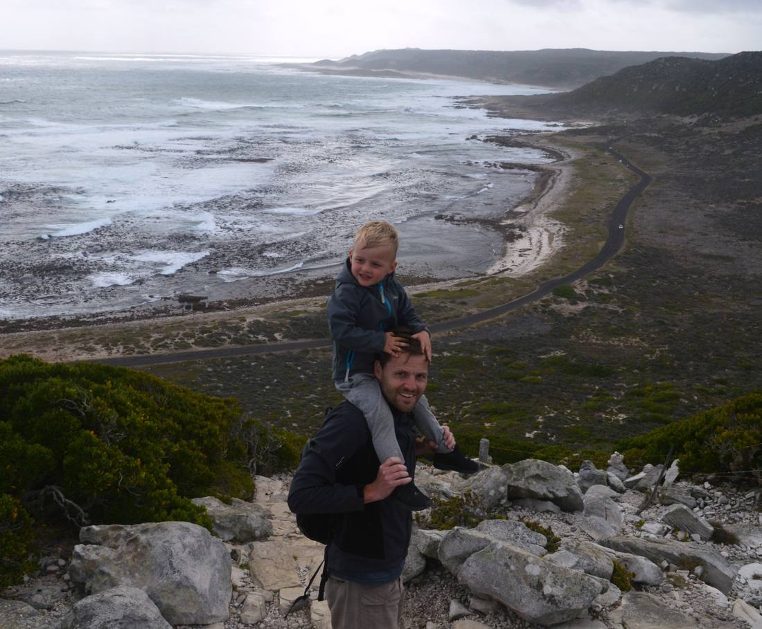 Een kind op de nek van zijn vader tijdens een wandeling langs de kust bij Kaapstad, Zuid-Afrika