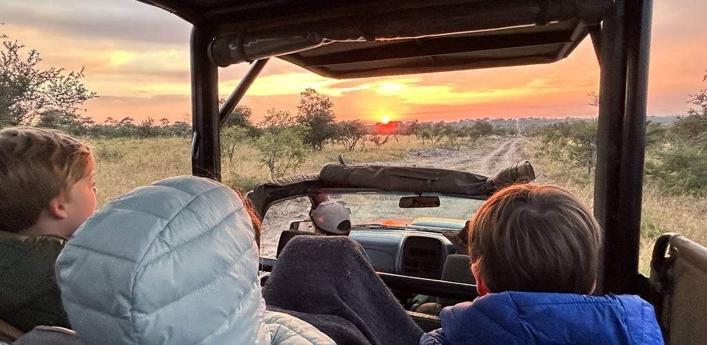 Kinderen in dikke jassen in de safarijeep bij zonsopkomst, Zuid-Afrika