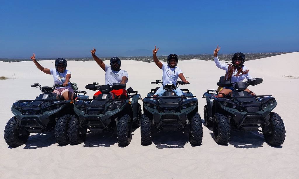 Reizigers steken hun hand op vanaf de quads op de witte duinen, Zuid-Afrika