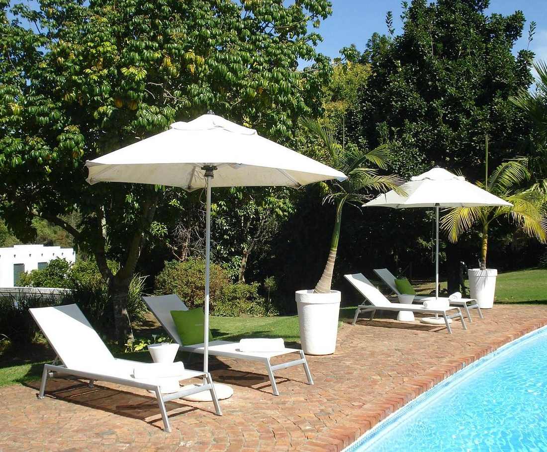 Ligbedden en parasols bij het zwembad tussen de oude bomen van het guesthouse in Swellendam, Zuid-Afrika