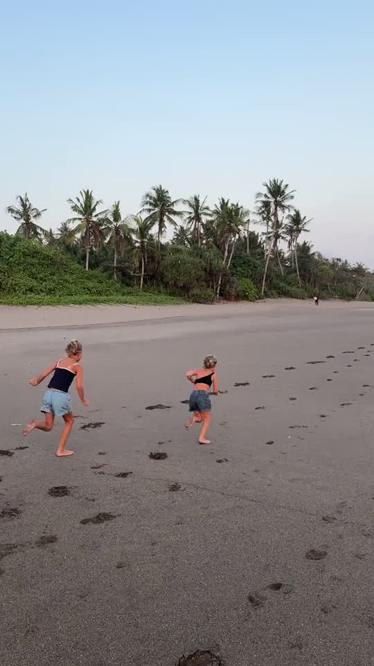Twee kinderen rennen over een zwart strand bij zonsondergang op Bali