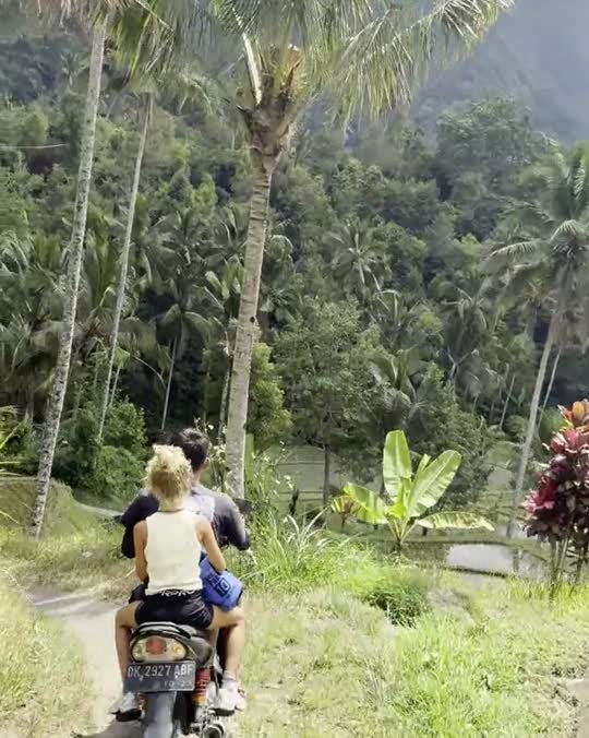 Twee reizigers op een scooter tussen de palmen en rijstvelden op Bali