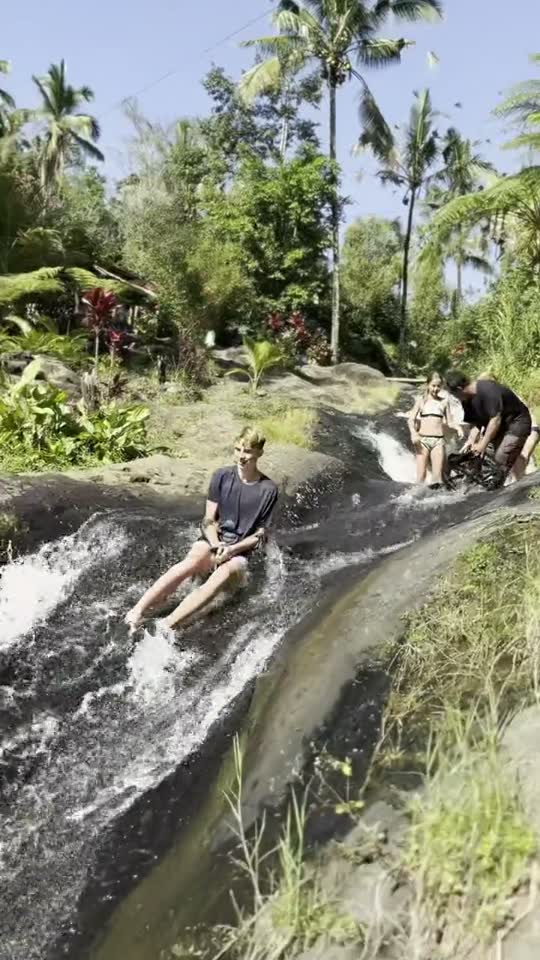 Een jongen glijdt in zijn T-shirt van een waterval af op Bali