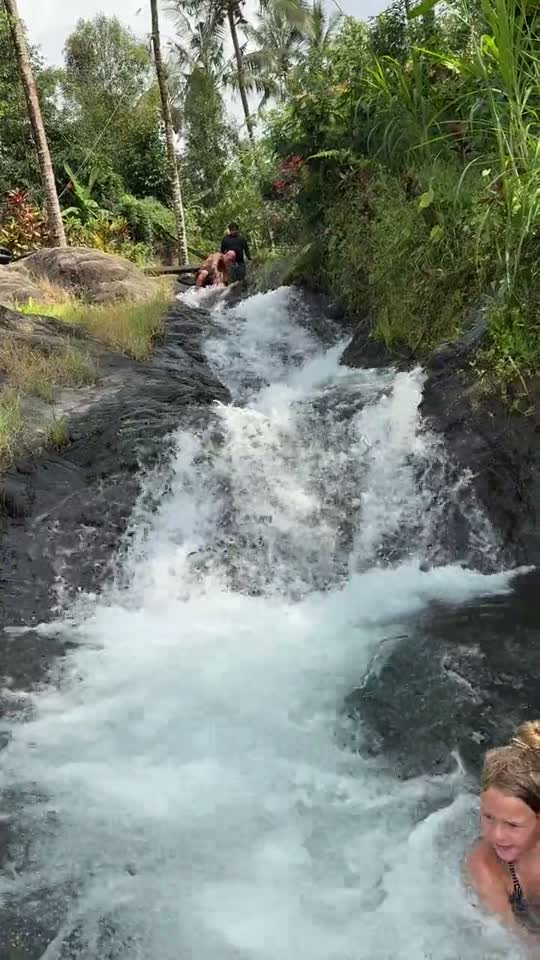 Kind zwemt in het water onder een bruisende waterval op Bali