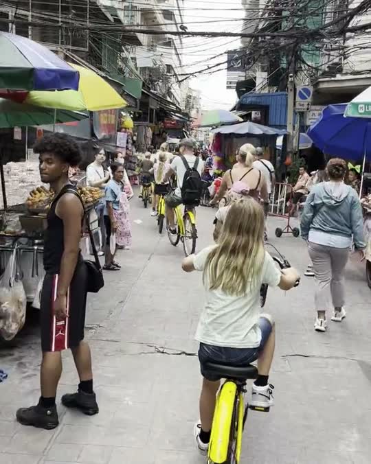 Kind op de fiets tussen de kraampjes in een drukke marktstraat in Bangkok