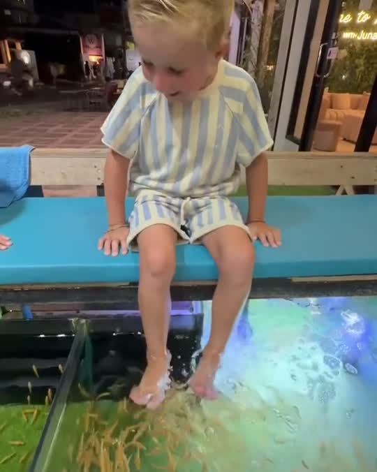 Een jongetje lacht als de visjes aan zijn voeten knabbelen in een visspa in Thailand