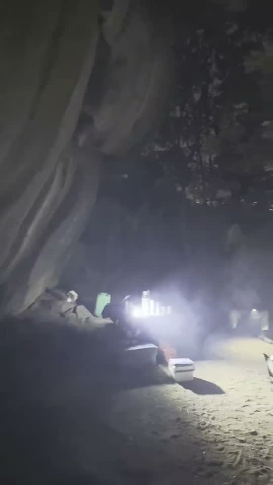 Een kamp onder een overhangende rots bij nacht, met het kampvuur en stoelen eromheen, zuidelijk Afrika